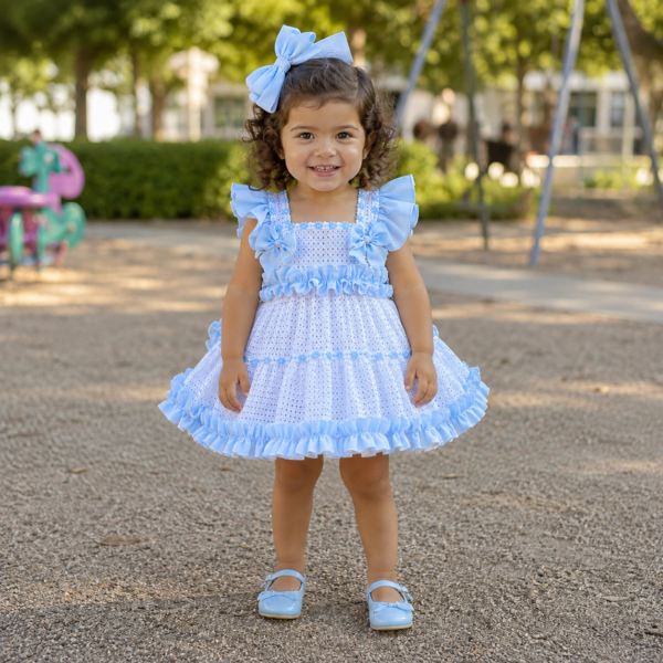 Niña con vestido blanco perforado y volantes celestes Ariadna posando en un parque